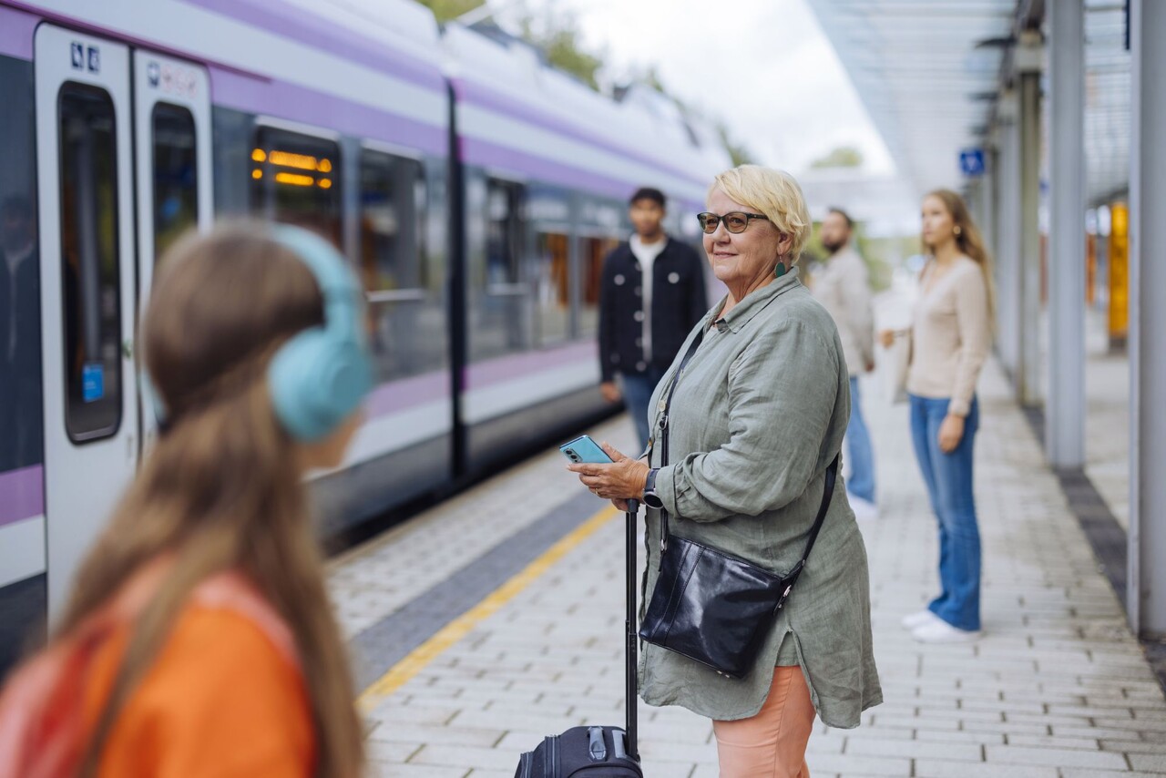 Eri ikäisiä ihmisiä lähijunaa odottamassa.