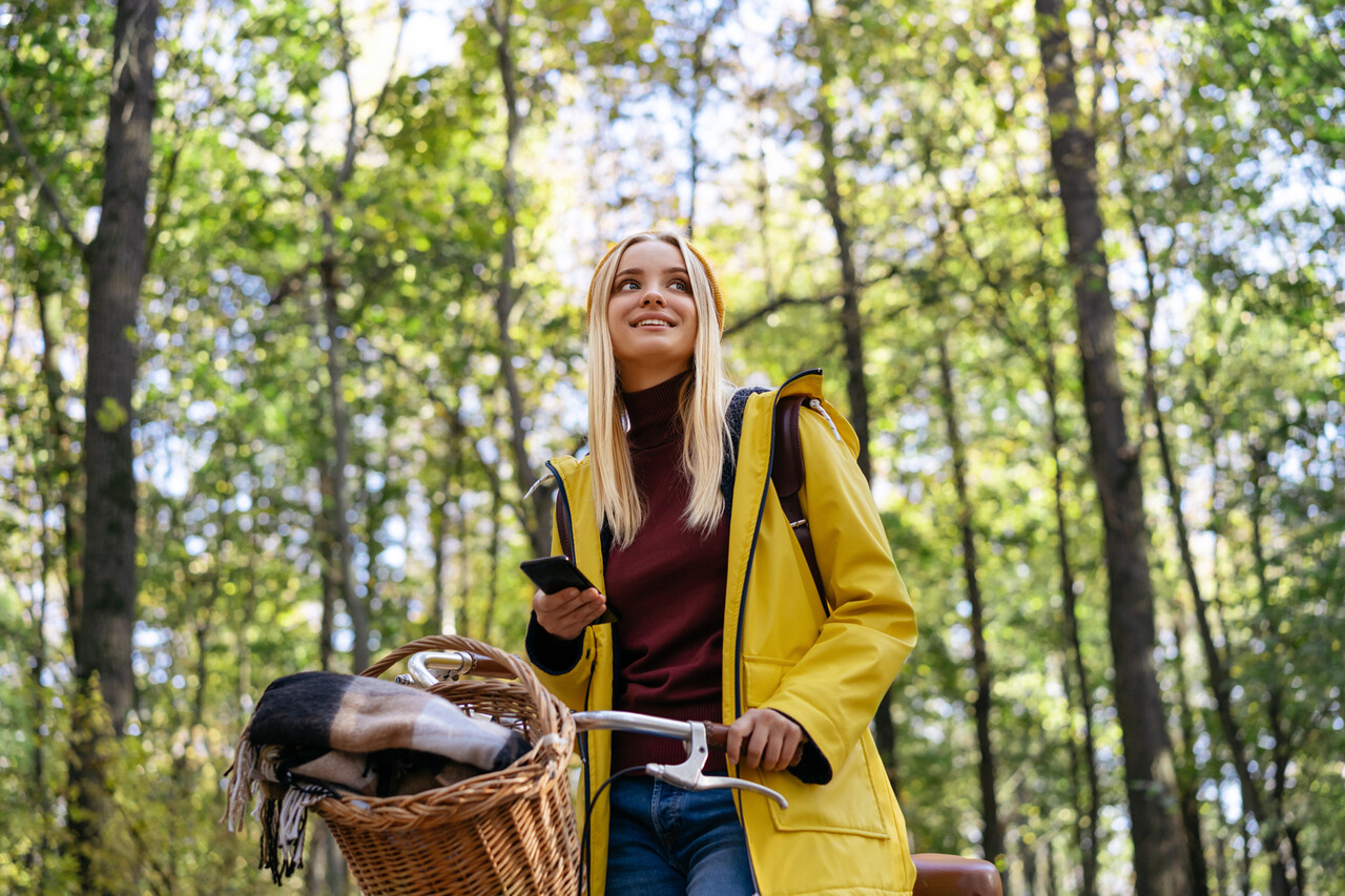 Nuori nainen seisoo metsässä pyörän vieressä kännykkä kädessä.